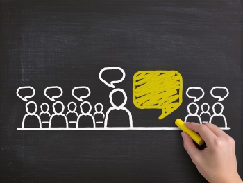 Hand drawing a group of people with speech bubbles and a hand drawing a yellow speech bubble on a blackboard image